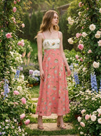 Woman in a coral A-line midi dress with spaghetti straps and a square neckline, posing in a garden with roses.