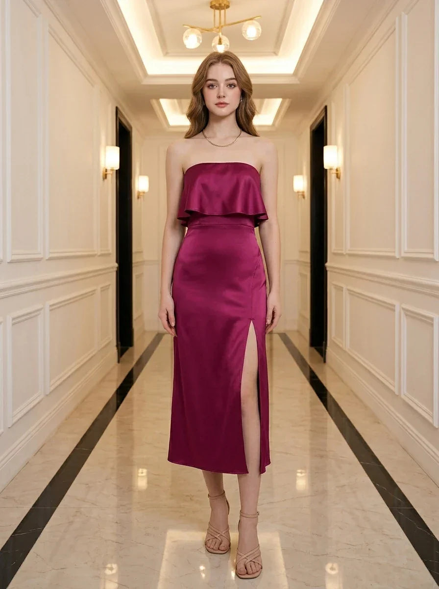 Woman wearing a strapless magenta satin midi dress with a high slit, standing in a hallway.