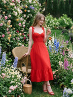 Woman wearing a red midi dress with tie straps and ruffle hem, sitting in a garden.