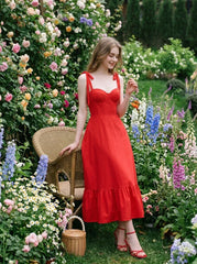 Woman wearing a red midi dress with tie straps and ruffle hem, sitting in a garden.