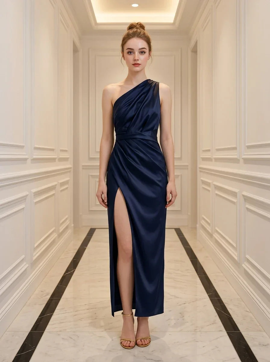 Woman wearing a navy blue satin one-shoulder gown with a high slit standing in a hallway
