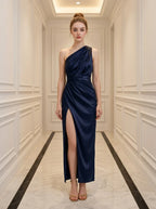 Woman wearing a navy blue satin one-shoulder gown with a high slit standing in a hallway