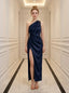 Woman wearing a navy blue satin one-shoulder gown with a high slit standing in a hallway