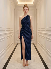 Woman wearing a navy blue satin one-shoulder gown with a high slit standing in a hallway
