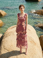Woman wearing a pink floral print maxi dress standing on a rock by the sea