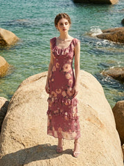 Woman wearing a pink floral print maxi dress standing on a rock by the sea