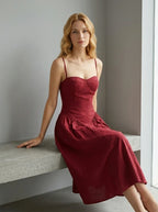 Woman wearing a deep red fit and flare midi dress with spaghetti straps, sitting on a concrete bench