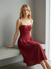 Woman wearing a deep red fit and flare midi dress with spaghetti straps, sitting on a concrete bench