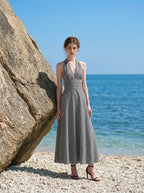 Woman wearing a black and white gingham halter maxi dress standing on a beach next to a large rock