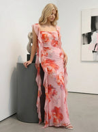 Woman leaning on a pedestal in a pink floral print maxi dress with ruffle trim