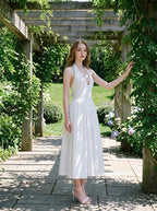 Woman in a white halter neck midi dress posing on a stone pathway under a wooden pergola with lush greenery.
