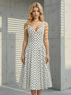 Woman in a white polka dot dress standing next to a concrete wall