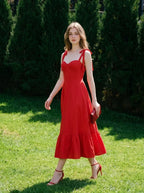 Woman wearing a red midi dress with tie straps and ruffle hem, walking on grass in a garden.
