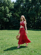 Woman wearing a red halter crop top and a tiered maxi skirt, walking in a grassy field