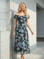 Woman standing in front of a building with blinds, wearing a black off-the-shoulder midi dress with a blue floral print