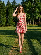 Woman walking in a grassy park, wearing a red and white floral print dress and red strappy heels