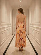 Woman standing in a hallway wearing a long, floral print, halter neck dress with an open back, viewed from the back.
