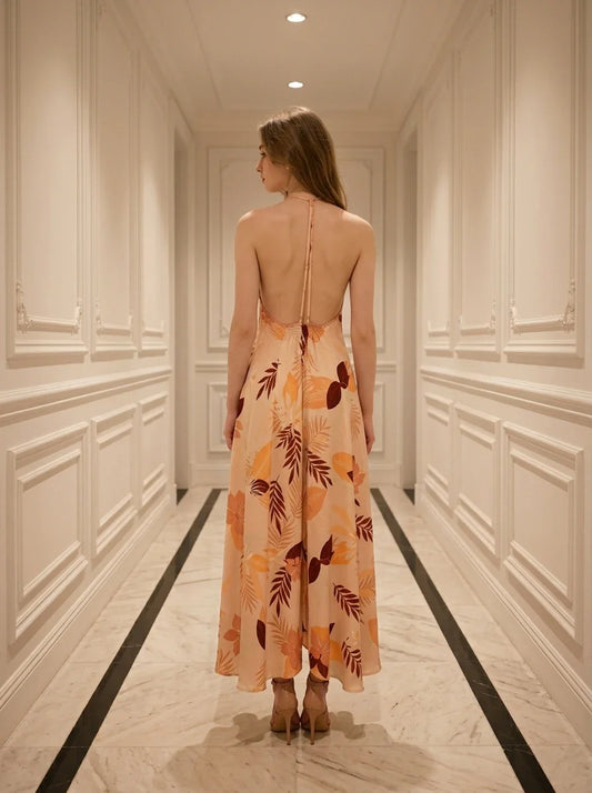 Woman standing in a hallway wearing a long, floral print, halter neck dress with an open back, viewed from the back.