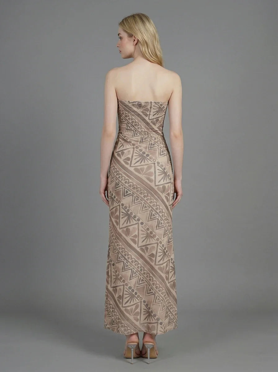 Woman wearing a strapless, patterned maxi dress standing against a grey background, back view.