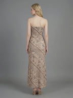 Woman wearing a strapless, patterned maxi dress standing against a grey background, back view.