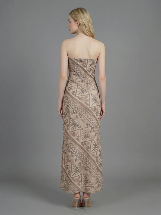Woman wearing a strapless, patterned maxi dress standing against a grey background, back view.