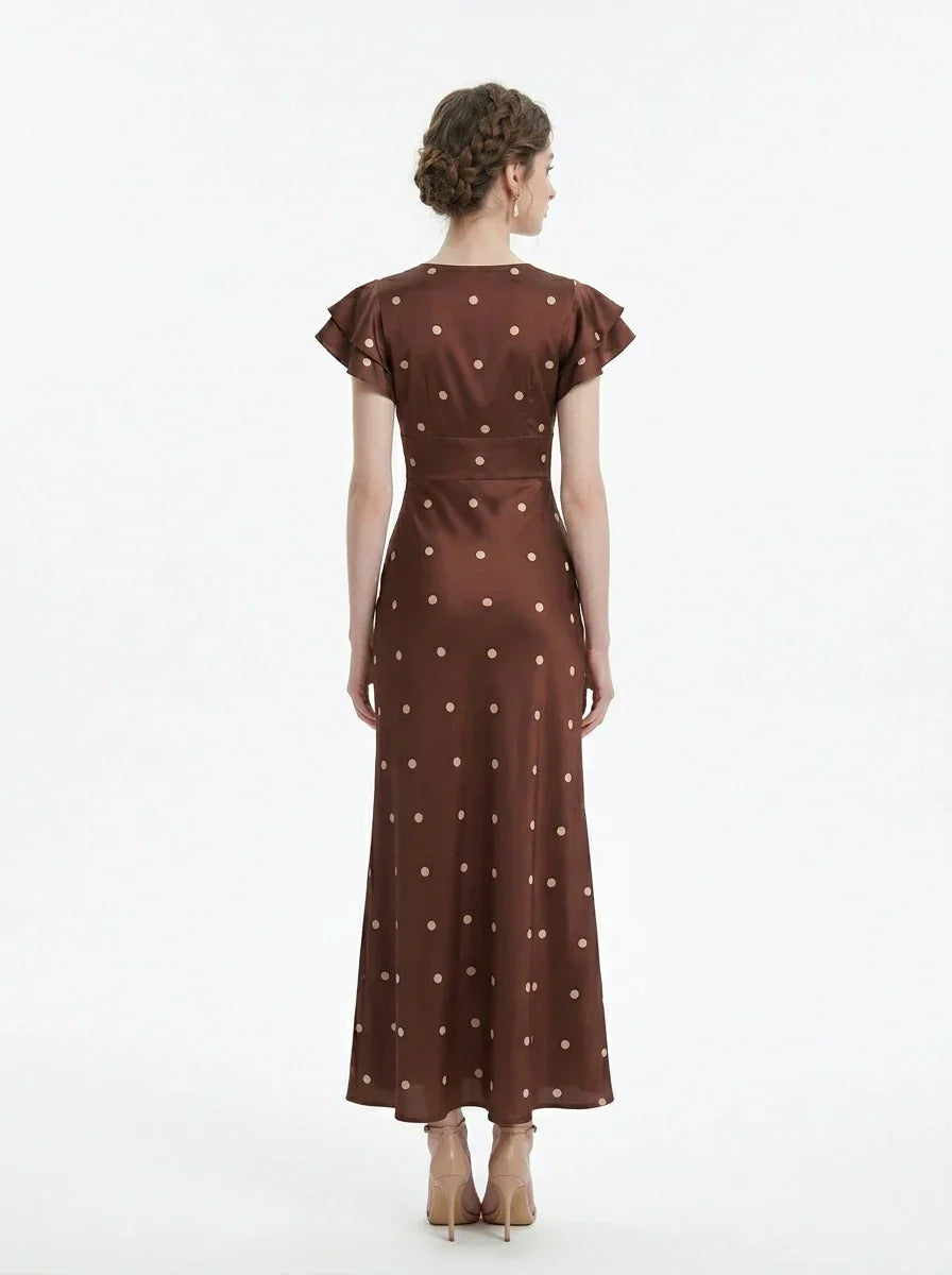 Back view of a woman wearing a brown polka dot midi dress with ruffled sleeves and a v-neckline, standing against a white background.