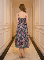 Rear view of a woman in a navy floral print midi dress with spaghetti straps and a peplum waist.