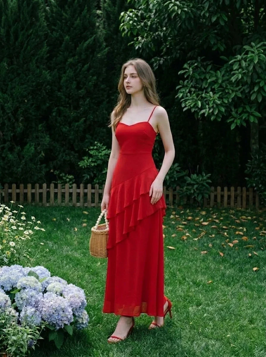 Woman wearing a red floor-length chiffon dress with tiered ruffles and spaghetti straps, standing in a garden with hydrangeas and a wicker basket.