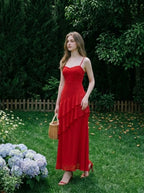 Woman wearing a red floor-length chiffon dress with tiered ruffles and spaghetti straps, standing in a garden with hydrangeas and a wicker basket.