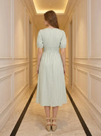 Back view of a woman in a light green and white striped midi dress with puff sleeves and a V-neck.