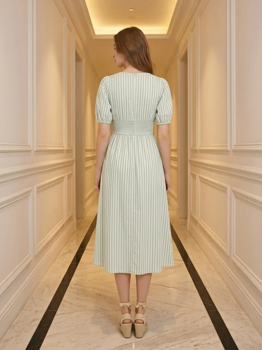 Back view of a woman in a light green and white striped midi dress with puff sleeves and a V-neck.