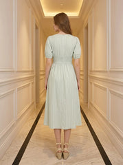 Back view of a woman in a light green and white striped midi dress with puff sleeves and a V-neck.