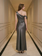 Back view of a woman wearing a floor-length grey satin one-shoulder dress with a high slit and bow accents.