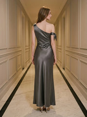 Back view of a woman wearing a floor-length grey satin one-shoulder dress with a high slit and bow accents.