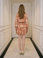 Back view of a woman wearing a floral print mini dress with long sleeves and a V-neck.