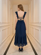Back view of a woman in a navy blue midi dress with a criss-cross back detail and tiered ruffled hem.