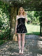 woman in black and white off-the-shoulder dress holding straw bag in garden
