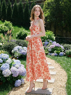 Woman wearing a cream and coral floral print halter midi dress, standing in a garden with hydrangeas.