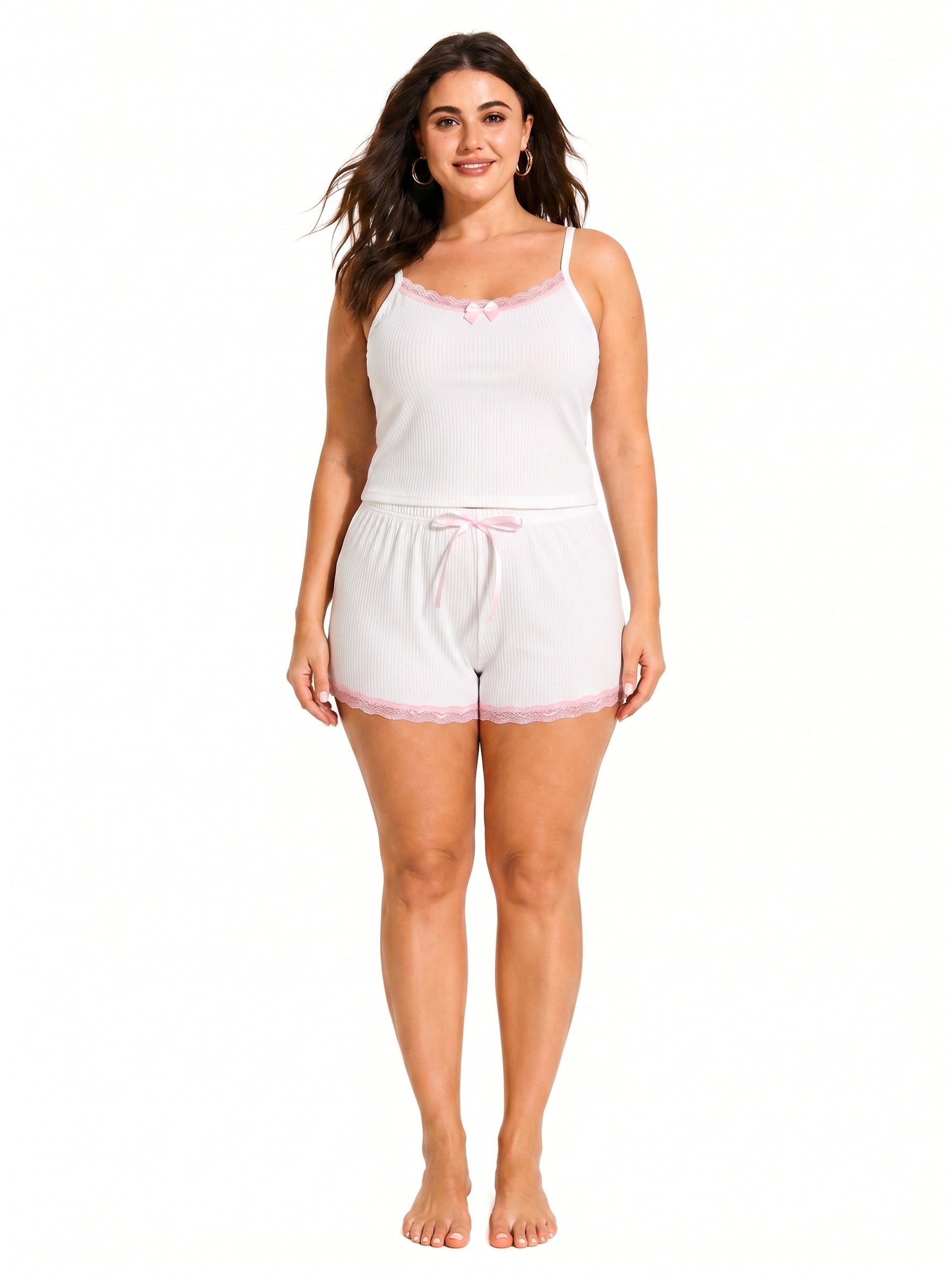 Woman wearing a white ribbed camisole and shorts pajama set with pink lace trim and bow accents.
