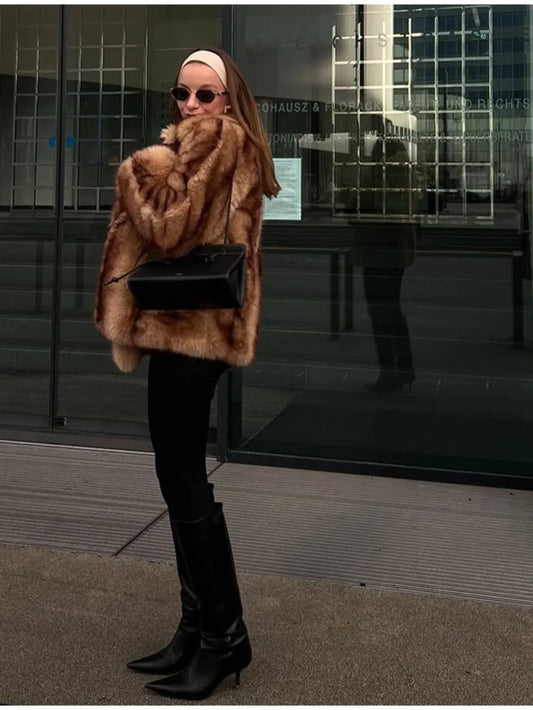Woman wearing a tan and brown faux fur cropped jacket with black pants and black boots.