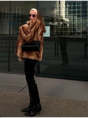 Woman wearing a tan and brown faux fur cropped jacket with black pants and black boots.