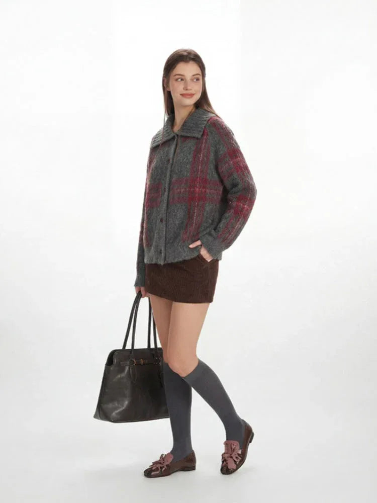 Side profile of a woman in a grey plaid knit jacket, brown mini skirt, and grey knee-high socks, carrying a black handbag.