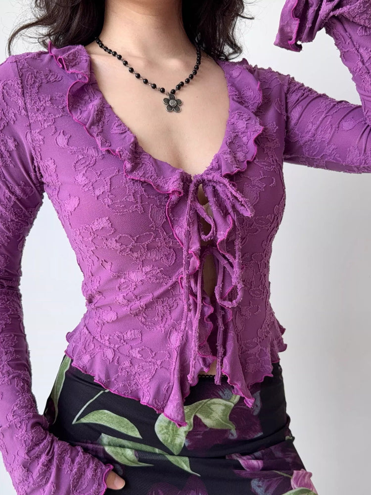 Woman in a purple floral lace long-sleeve top with ruffles and a tie-front, paired with a floral skirt.