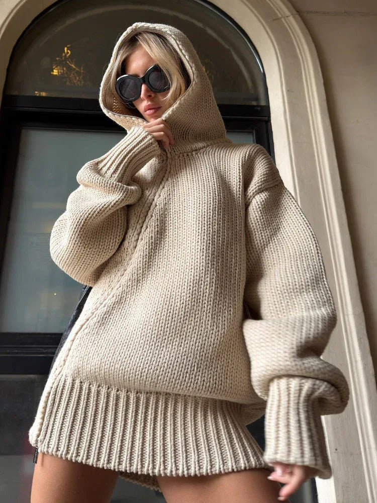 Woman wearing a beige oversized knit hooded sweater dress with black sunglasses.