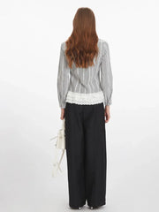 Rear view of a woman wearing a long-sleeved plaid collared shirt with a white ruffled hem and black wide-leg pants.