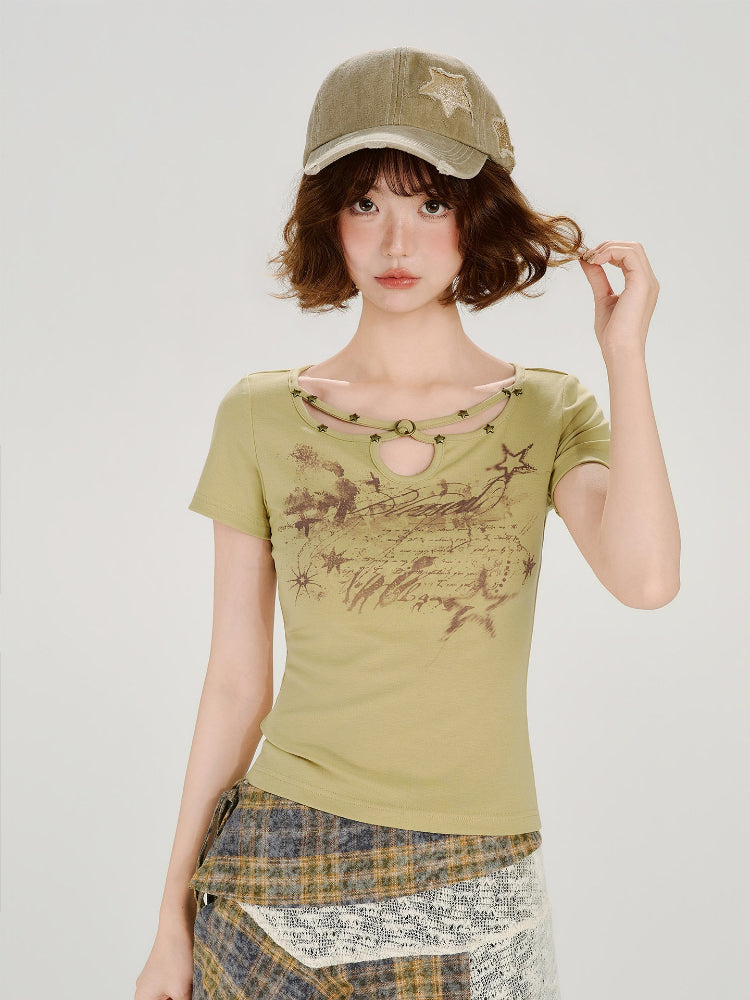 Model wearing a light green short-sleeve t-shirt with a cutout neckline and star details, paired with an asymmetrical plaid skirt and a khaki baseball cap.