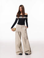 Full-body shot of a woman in a black off-the-shoulder knit top with a decorative yoke and loose-fitting beige cargo pants.