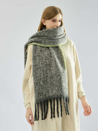Woman modeling a grey, textured knit scarf with fringe and lime green trim, partially covering her face.