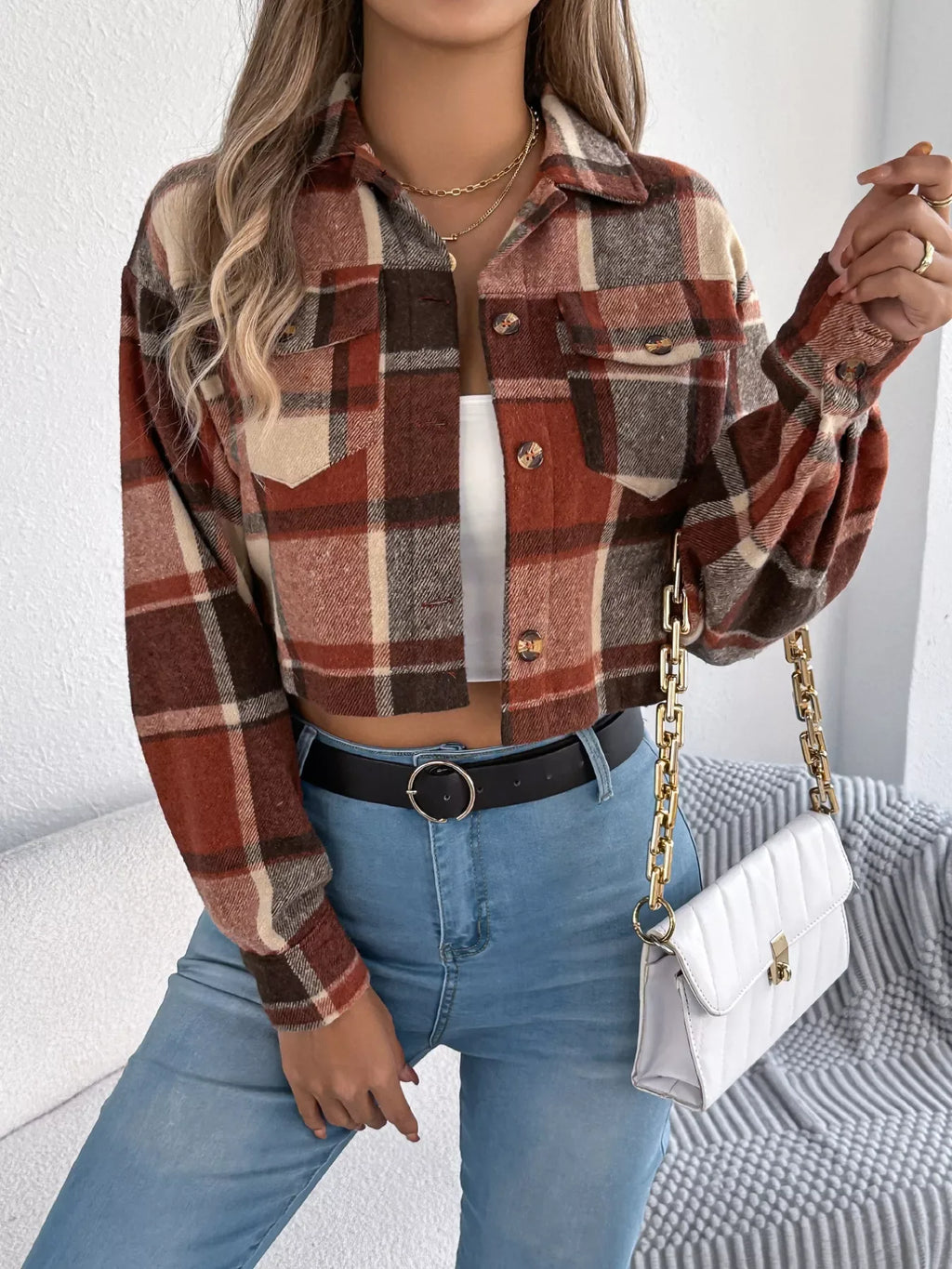 Model posing with a white quilted handbag while wearing a cropped plaid jacket, white tank top, and blue jeans.