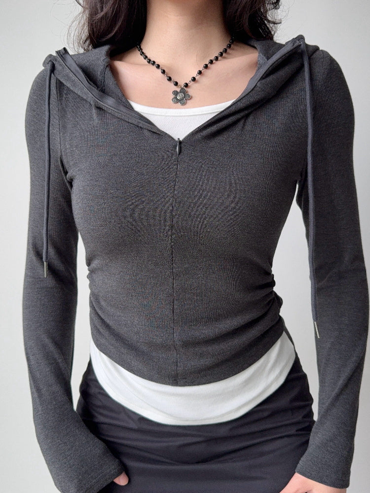 Front view of a woman in a dark grey hooded zip-up top, white tank, and black skirt, showcasing the ruched side detail.